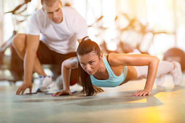Woman doing push ups under supervision of a trainer picture id519399268